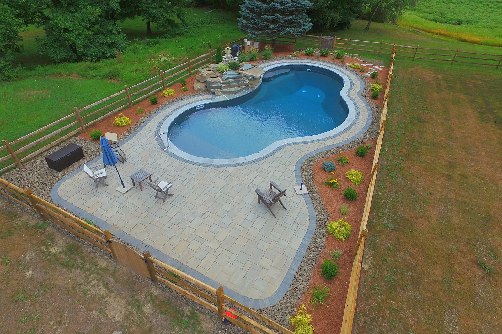 Finished freeform inground pool with rock waterfall and split-rail fence built by Chaffee's
