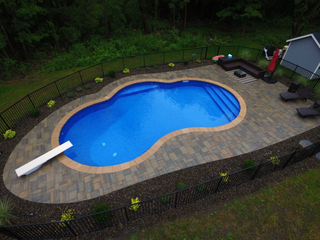 Kidney-shaped inground pool with diving board and paver patio by Chaffee's