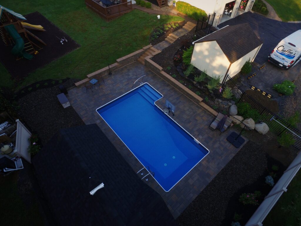L-shaped inground pool with retaining wall and paver patio by Chaffee's