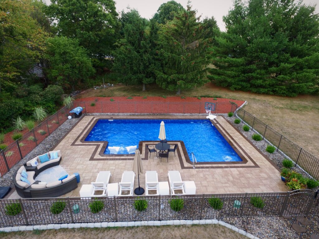 L-shaped pool with tanning ledge, outdoor seating and fenced patio by Chaffee's