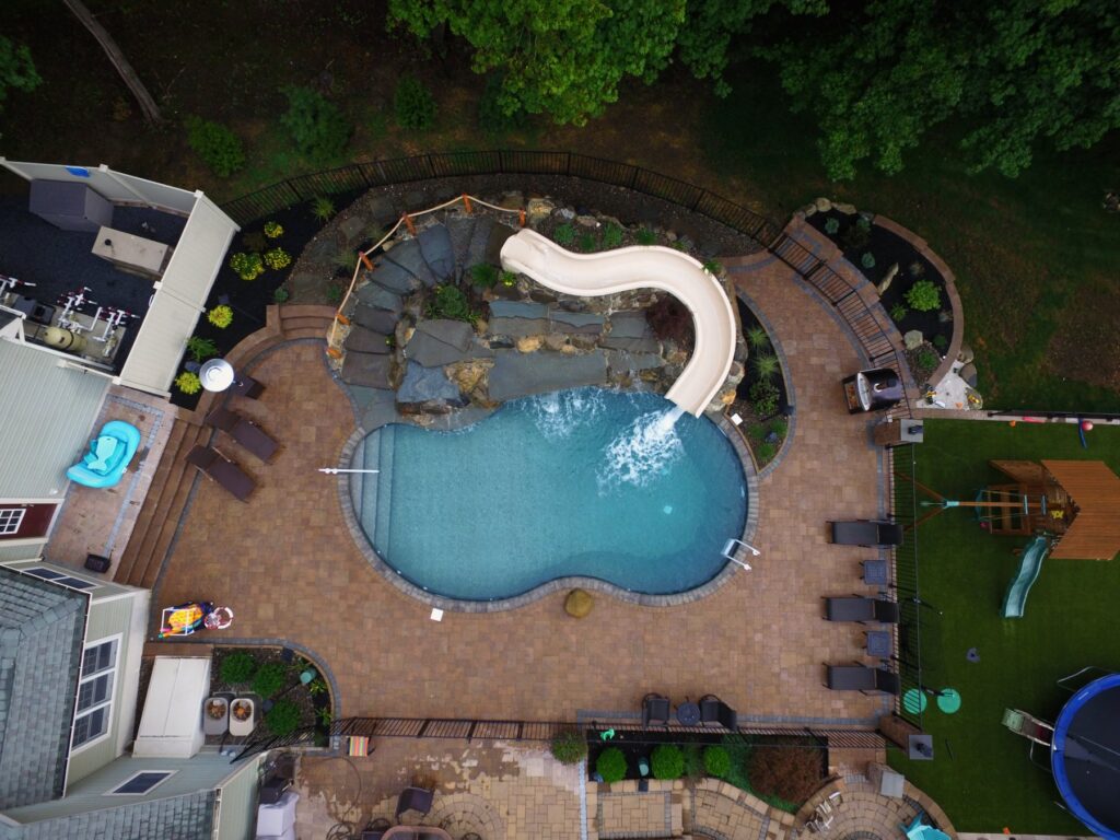 Aerial view of a pool with waterfall, slide and paver patio by Chaffee's
