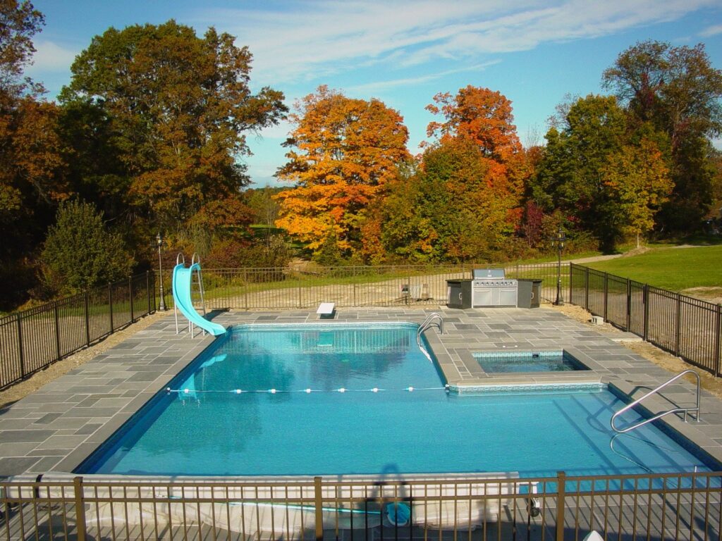 Rectangle inground pool with attached spa, slide and bluestone patio in autumn by Chaffee's